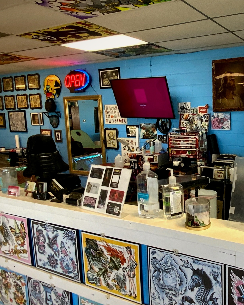 The front reception counter with OPEN neon, a TV, and rows of flash panels