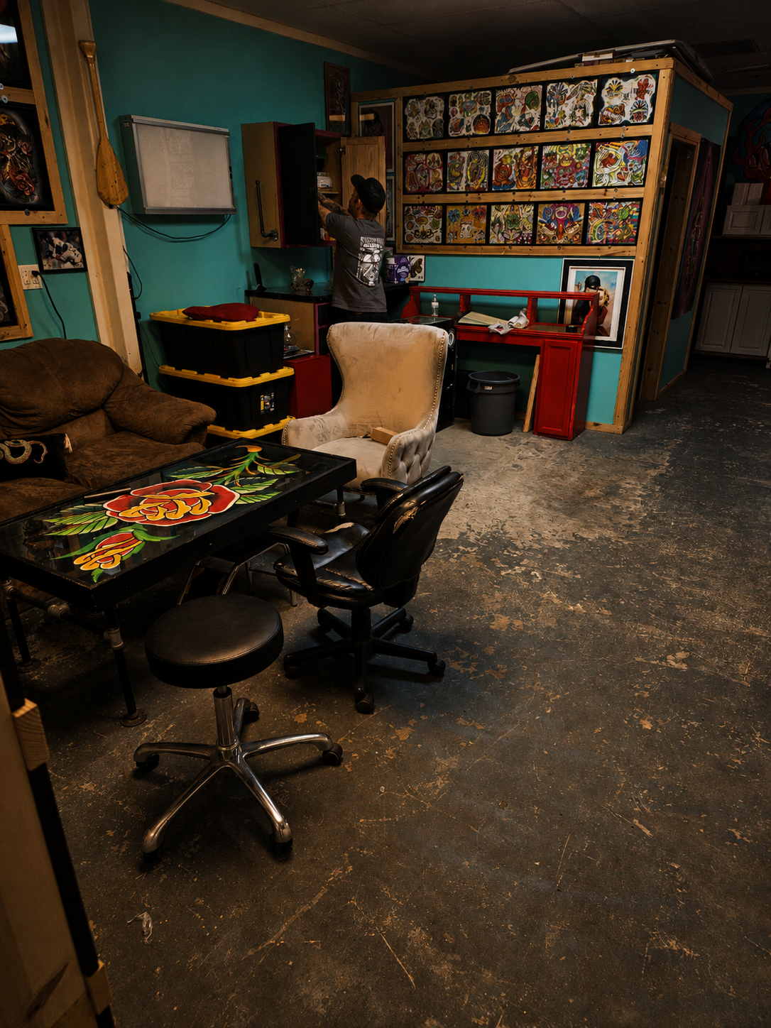 An artist arranging flash on the wall of a teal-walled workspace at A Holy Grail Tattoo