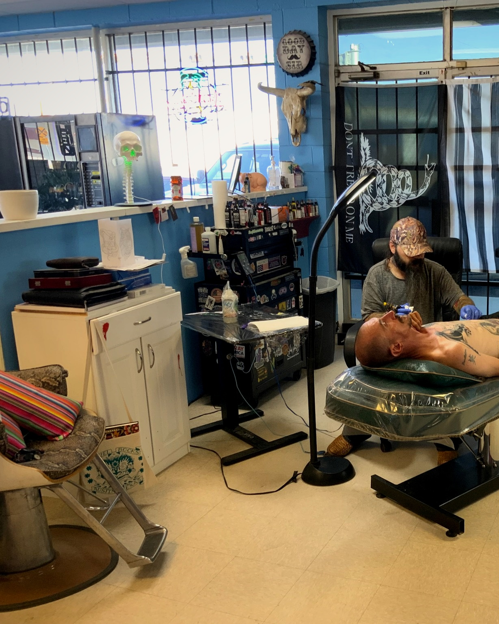 A Holy Grail artist tattooing a client reclined on the table