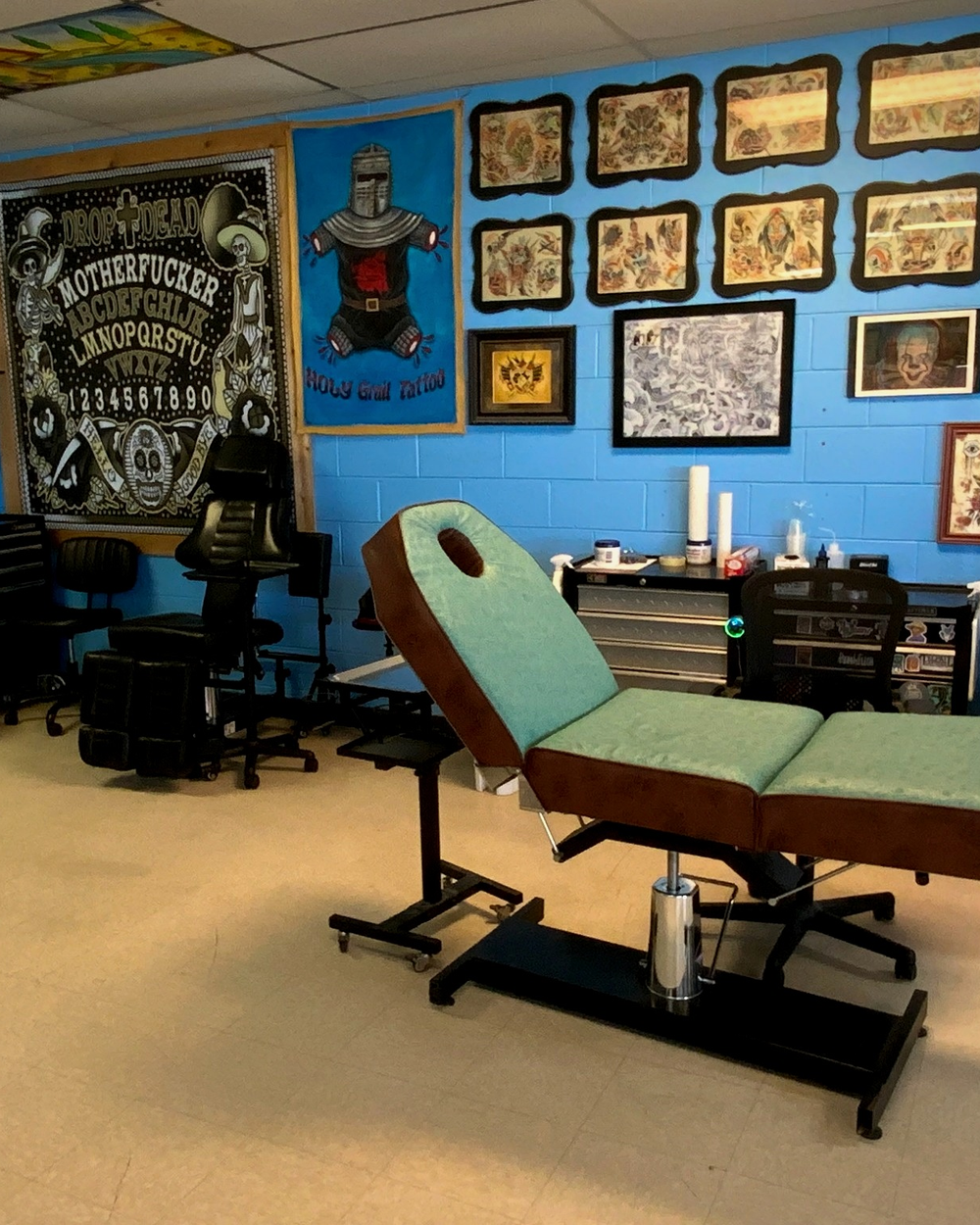 A mint-and-brown tattoo chair beneath a wall of traditional flash and a Ouija tapestry