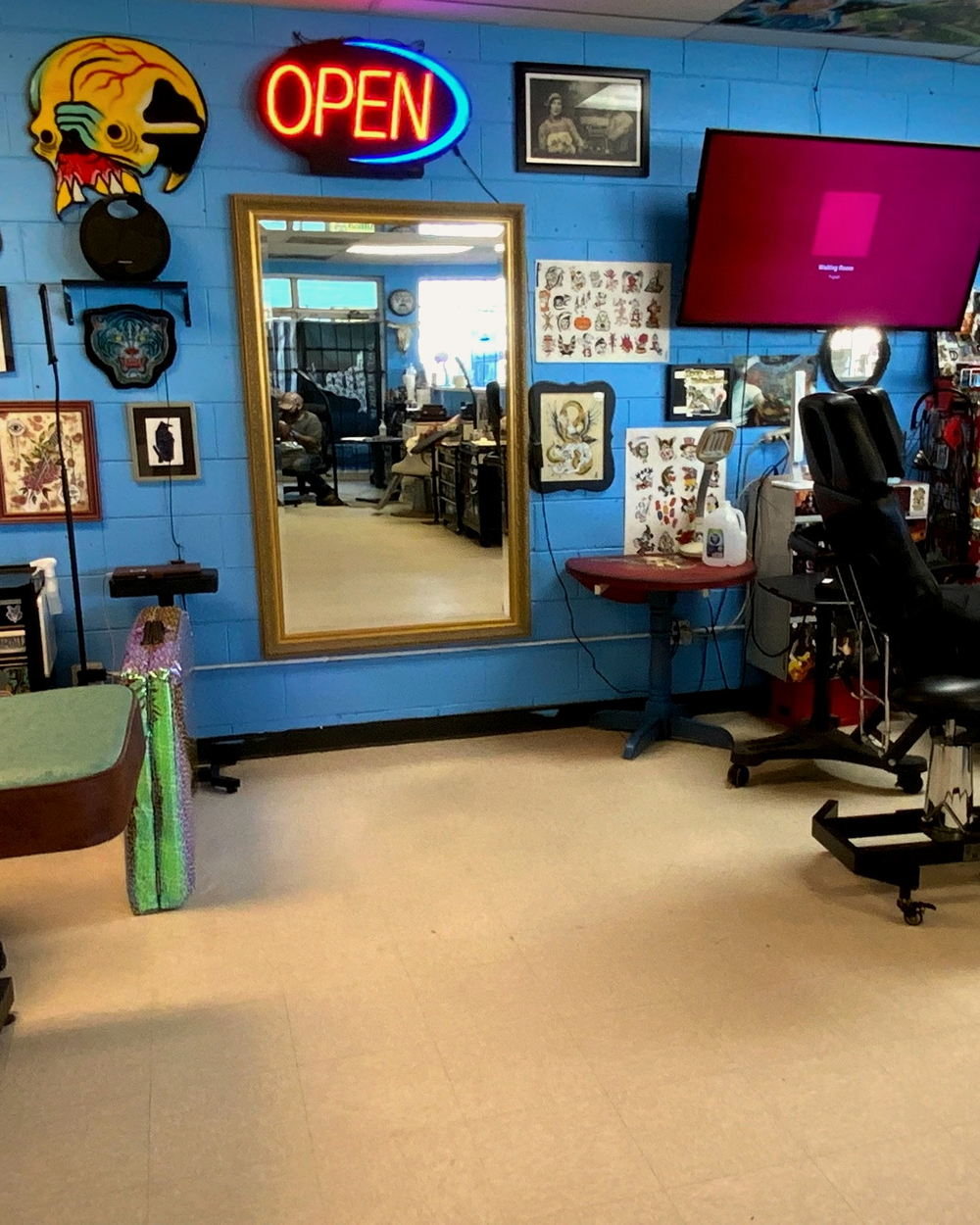A tattoo station with a gold-framed mirror, glowing OPEN sign, and flash-covered walls